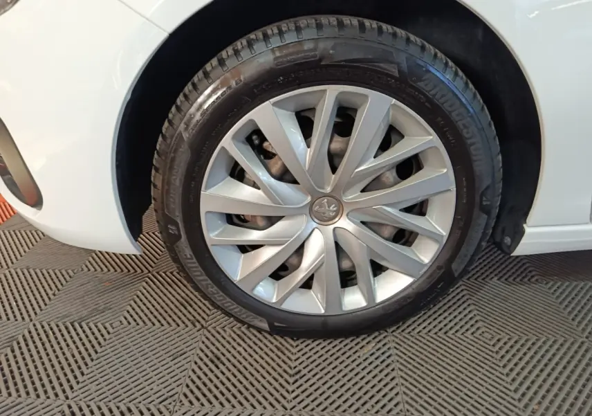 Gros plan sur la roue avant gauche d'une Peugeot 308 blanche, mettant en valeur la jante argentée et le logo lion central.