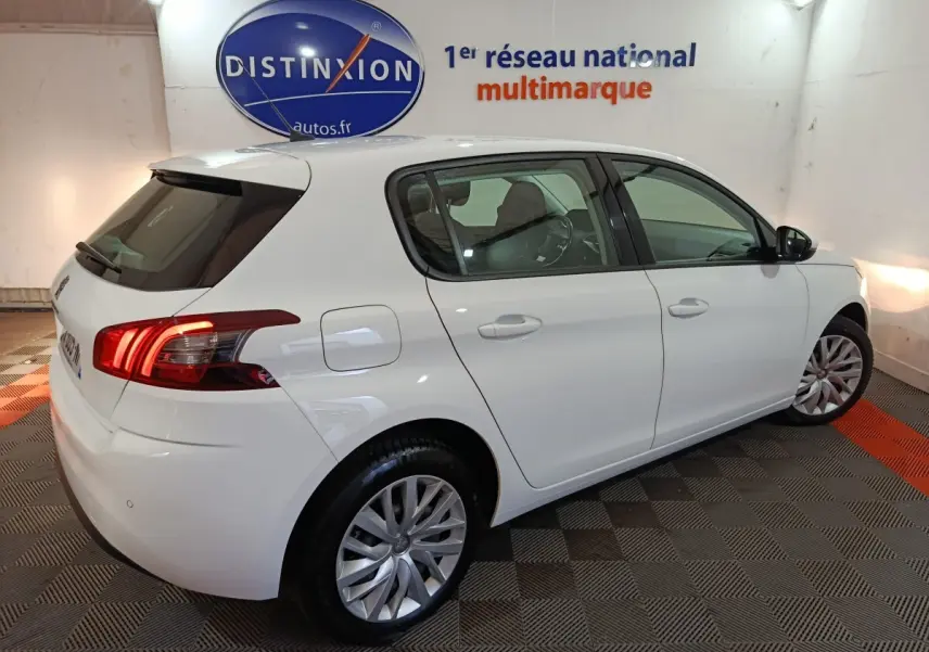 Peugeot 308 blanc vue 3/4 arrière droit en intérieur, feux arrière allumés et jantes alliage visibles