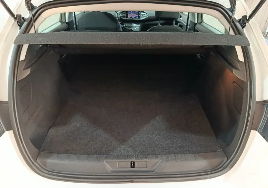 Coffre ouvert vue arrière d'une Peugeot 308 blanche, montrant un espace de chargement propre et spacieux.
