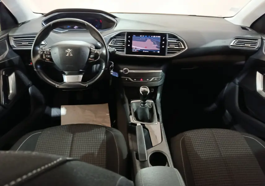 Vue intérieure frontale du poste de conduite de la Peugeot 308 blanche, avec volant cuir et écran tactile central allumé.