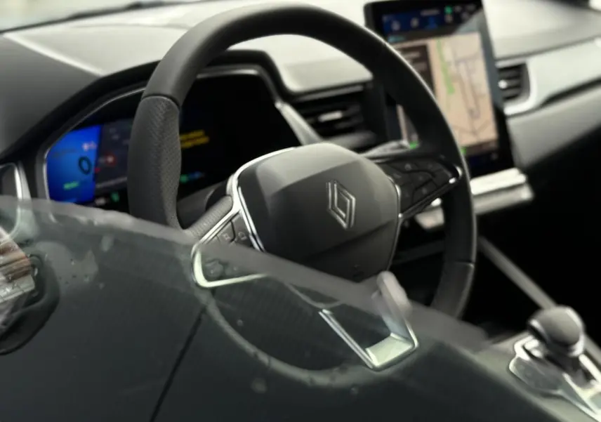 Vue intérieure rapprochée du volant cuir noir et de l’écran tactile vertical du tableau de bord du Renault Symbioz gris Rafale.