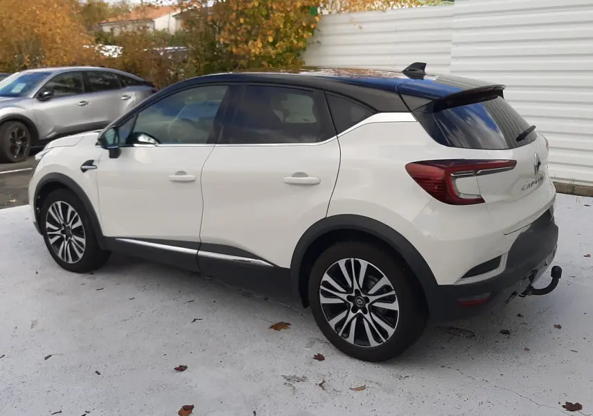 Renault Captur blanc avec toit noir vu de trois quarts arrière côté gauche, stationné sur sol clair.