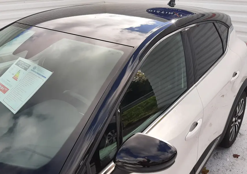 Vue 3/4 avant droit du Renault Captur blanc avec toit noir brillant et rétroviseur noir.