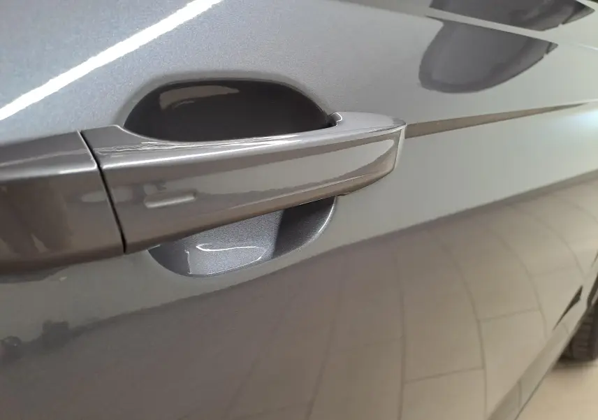 Poignée de porte côté gauche en gros plan sur Volkswagen Taigo gris cendré métallisé avec reflet de lumière.