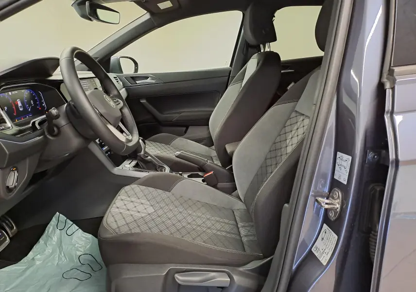 Vue intérieure côté conducteur du Volkswagen Taigo gris cendré 2025, sièges tissu à motifs géométriques et tableau de bord digital.