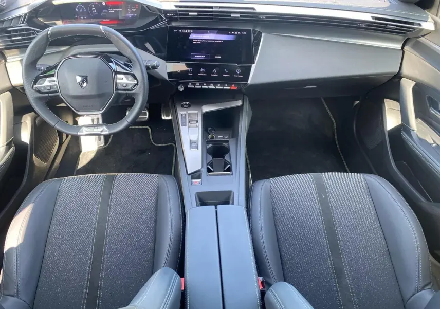 Intérieur Peugeot 308 1.2 hybrid 145 GT 2025, vue avant centrée sur tableau de bord, volant compact et sièges tissu cuir gris.