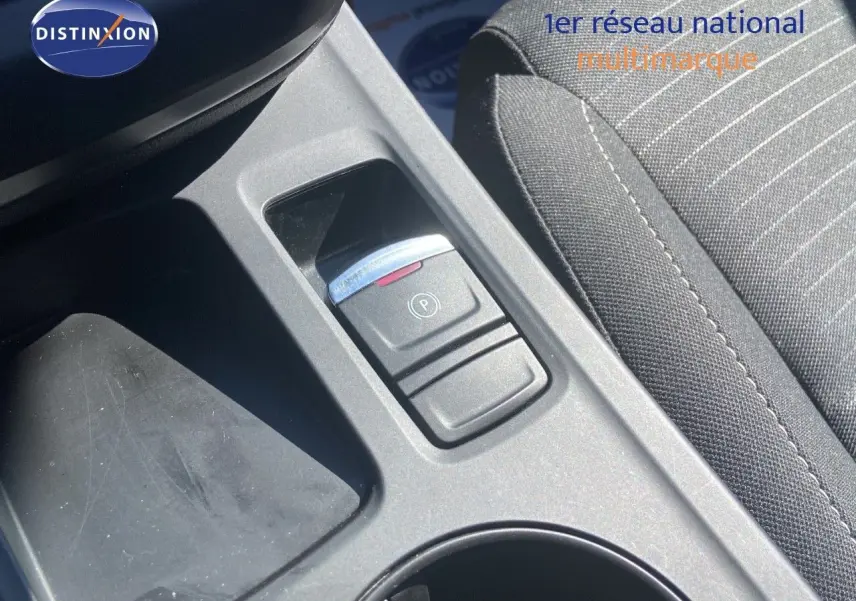 Gros plan sur la console centrale noire avec bouton de frein à main électronique et siège tissu gris à rayures.