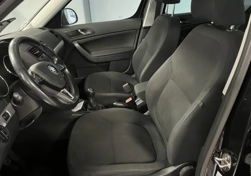 Vue intérieure côté conducteur du Skoda Yeti 2015 avec sièges tissu noirs et volant multifonctions cuir.