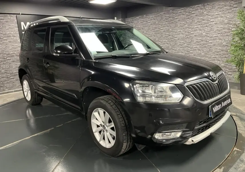 Vue 3/4 avant droite d'un Skoda Yeti noir avec jantes alliage et barres de toit argentées en intérieur showroom.