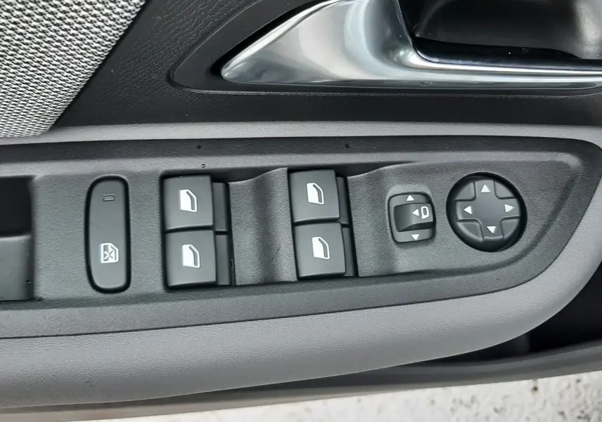 Gros plan sur la commande des vitres et rétroviseurs côté gauche d'une Citroën C4 blanche 2025 avec poignée argentée.