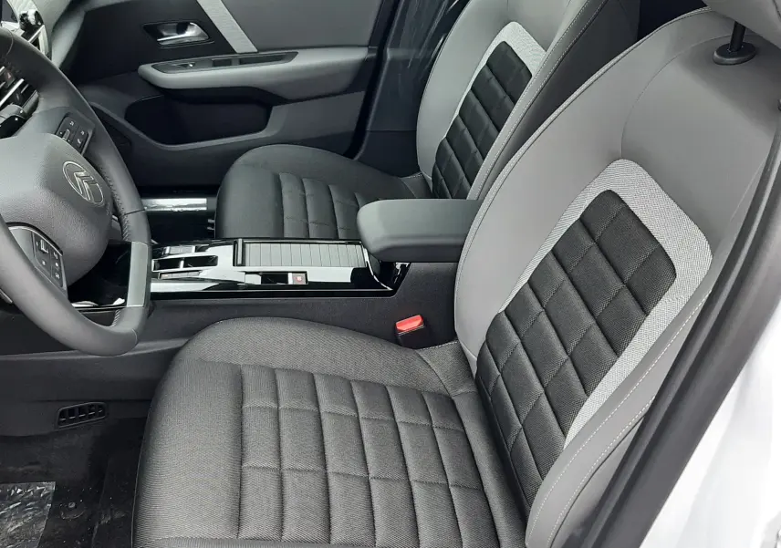 Intérieur avant droit d'une Citroën C4 2025 hybride, sièges gris à inserts noirs et console centrale brillante noire.