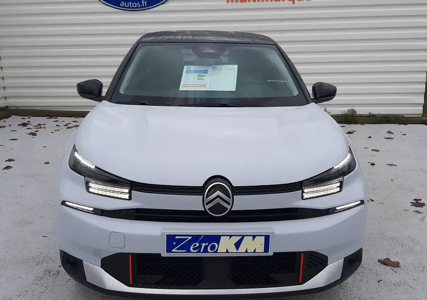 Vue frontale d'une Citroën C4 2025 blanc Okenite avec toit noir Perla, feux LED et plaque Zéro KM visible.