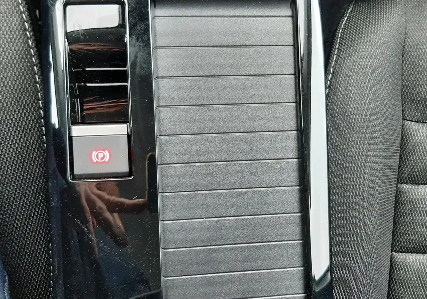 Gros plan sur la console centrale noire brillante avec frein à main électronique et accoudoir du Citroën C4 hybride 2025.