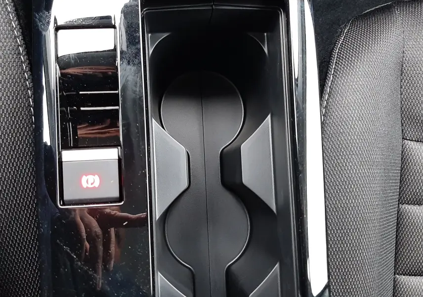 Gros plan sur la console centrale noire brillante avec porte-gobelets et frein à main électrique de la Citroën C4 hybride 2025.