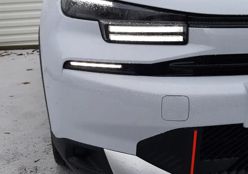 Gros plan sur l'avant gauche blanc Okenite avec toit noir Perla de la Citroën C4 hybride 2025, feux LED allumés.