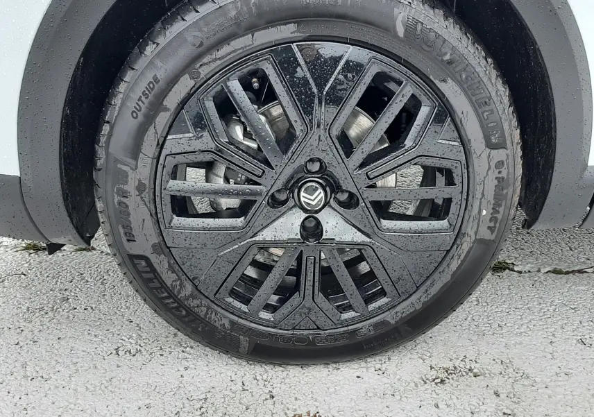 Gros plan sur la roue avant gauche du Citroën C4 blanc Okenite avec jante noire au design géométrique et logo Citroën central.