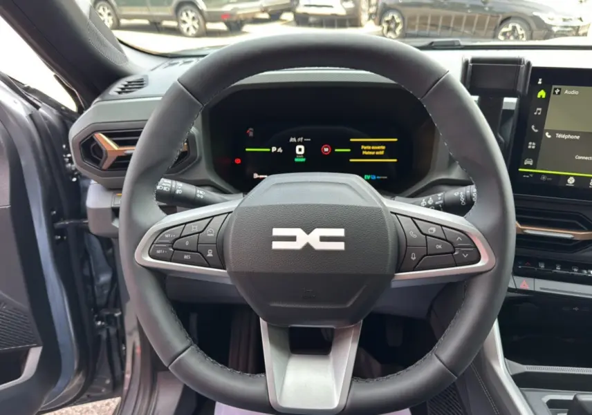 Vue intérieure centrée sur le volant cuir noir du Dacia Bigster Hybrid 155 Extreme Plus avec tableau de bord digital allumé.