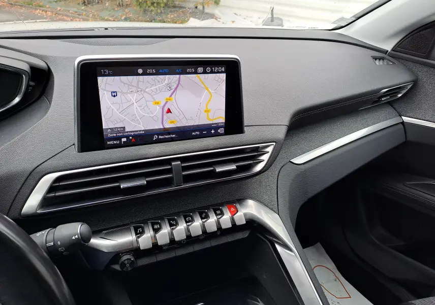 Vue intérieure du tableau de bord du Peugeot 3008 blanc, avec écran tactile affichant la navigation et commandes piano clés argentées.