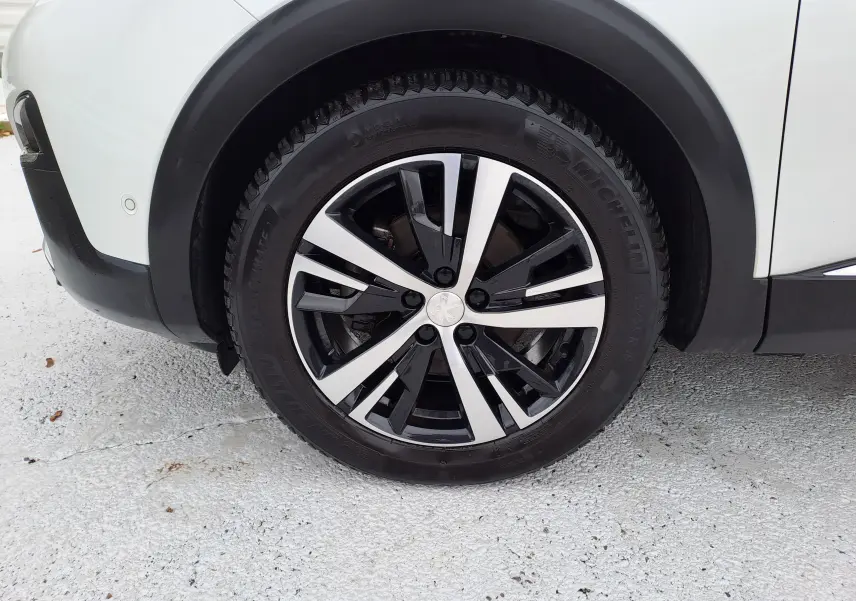 Gros plan sur la roue avant gauche du Peugeot 3008 blanc, mettant en valeur la jante alliage bicolore et le pneu Michelin.