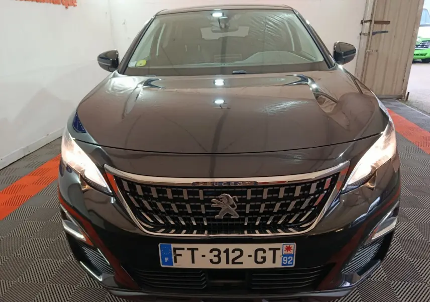 Vue frontale d'un Peugeot 3008 noir avec calandre chromée et phares allumés en intérieur.
