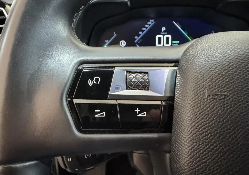 Gros plan sur les commandes gauche du volant cuir du DS7 Crossback gris foncé, avec affichage numérique en arrière-plan.