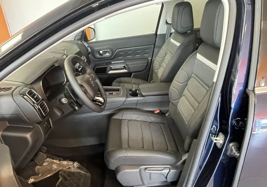 Vue intérieure côté conducteur du Citroën C5 Aircross hybride 2025 bleu foncé, avec sièges tissu/TEP et volant cuir.