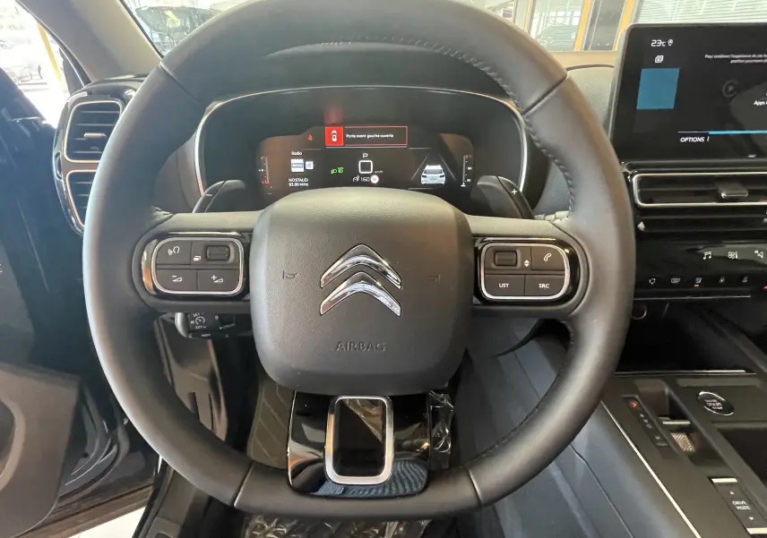 Vue intérieure centrée sur le volant cuir noir du Citroën C5 Aircross hybride 2025 avec tableau de bord digital et écran tactile.