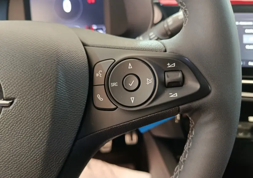 Gros plan sur les commandes gauche du volant cuir noir de l’Opel Corsa rouge 2023, avec boutons multifonctions.