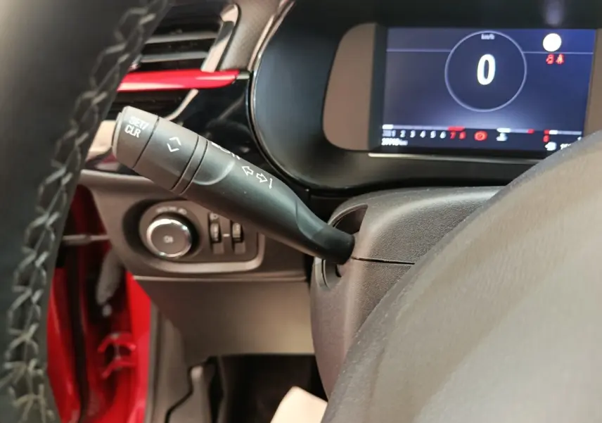 Gros plan sur la manette de clignotant et le combiné d'instruments numérique d'une Opel Corsa rouge, vue côté conducteur.