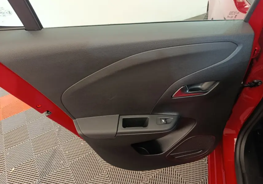 Vue rapprochée de la porte intérieure côté gauche d’une Opel Corsa rouge, avec poignée argentée et commande de fenêtre.