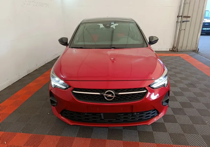 Vue frontale d'une Opel Corsa rouge 2023 avec calandre noire et phares LED allumés dans un garage.