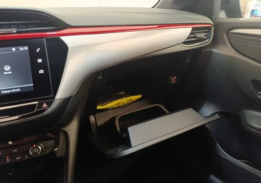 Intérieur de l’Opel Corsa rouge 2023, vue côté passager sur la boîte à gants ouverte et tableau de bord avec écran tactile.