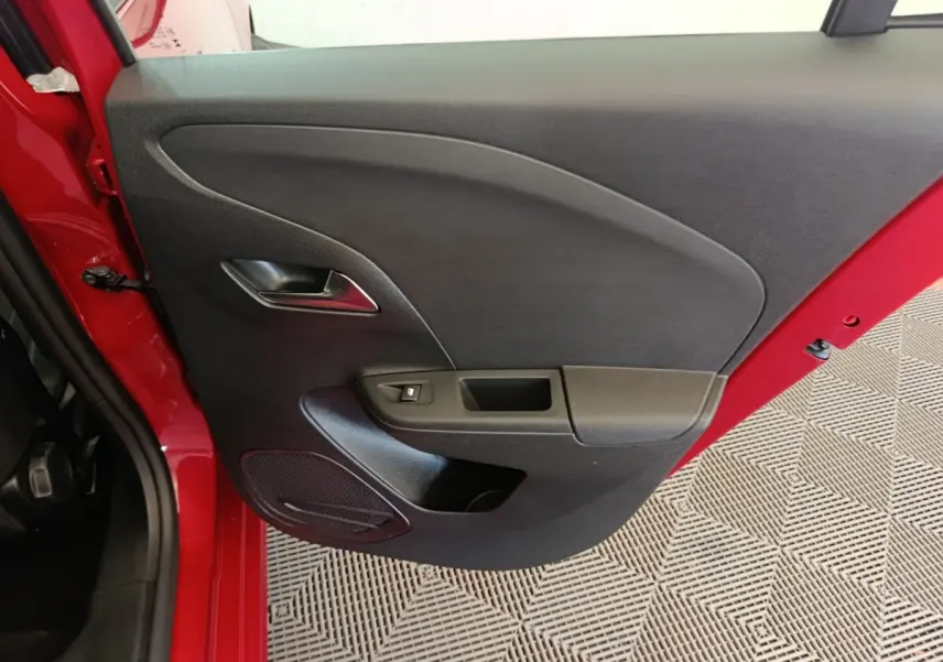 Vue rapprochée de la porte arrière gauche noire d’une Opel Corsa rouge 2023, avec poignée et commande de vitre.