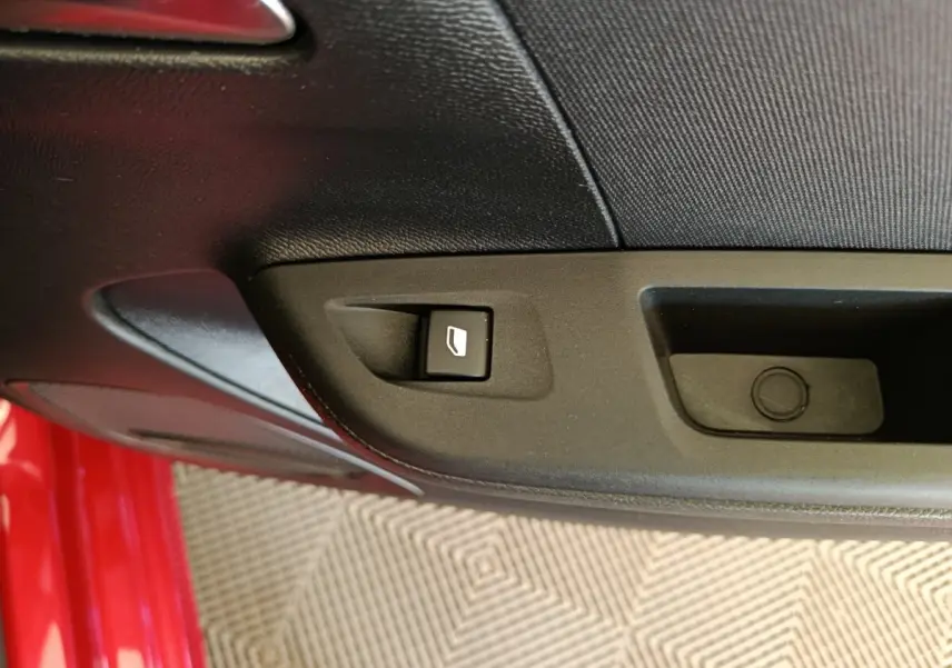 Gros plan sur la commande de lève-vitre côté conducteur d’une Opel Corsa rouge, intérieur noir.