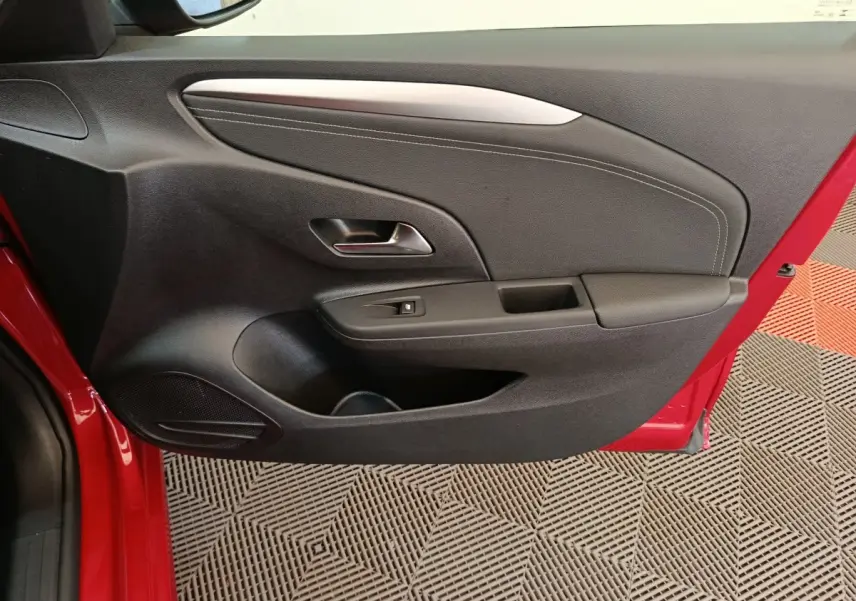 Vue rapprochée de la porte intérieure côté gauche rouge de l’Opel Corsa 1.2 Turbo 2023 avec poignée et commande de vitre.