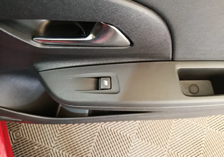 Détail de la poignée intérieure et commande de vitre sur la porte côté gauche d’une Opel Corsa rouge.