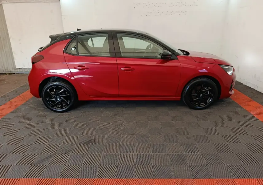Vue de profil côté gauche d'une Opel Corsa rouge 2023 avec toit noir et jantes noires brillantes.