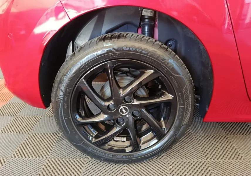 Gros plan sur la roue avant gauche noire brillante d’une Opel Corsa rouge 2023, avec logo Opel au centre.