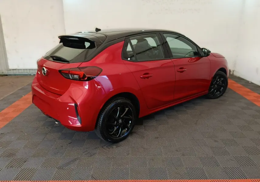 Opel Corsa rouge vue 3/4 arrière côté gauche, toit noir et jantes noires brillantes dans un garage.