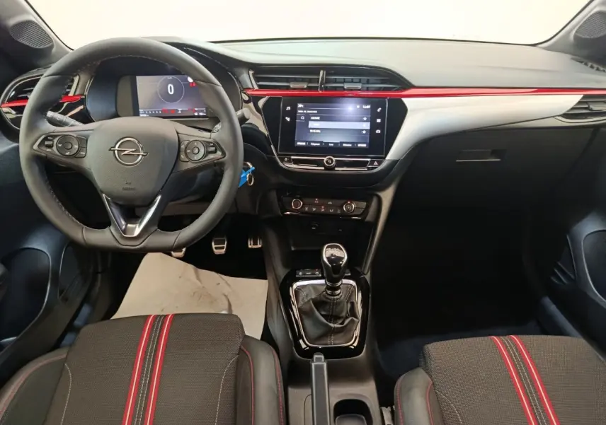 Vue intérieure avant de l’Opel Corsa rouge 2023, volant multifonctions, écran tactile central et levier de vitesse manuel.