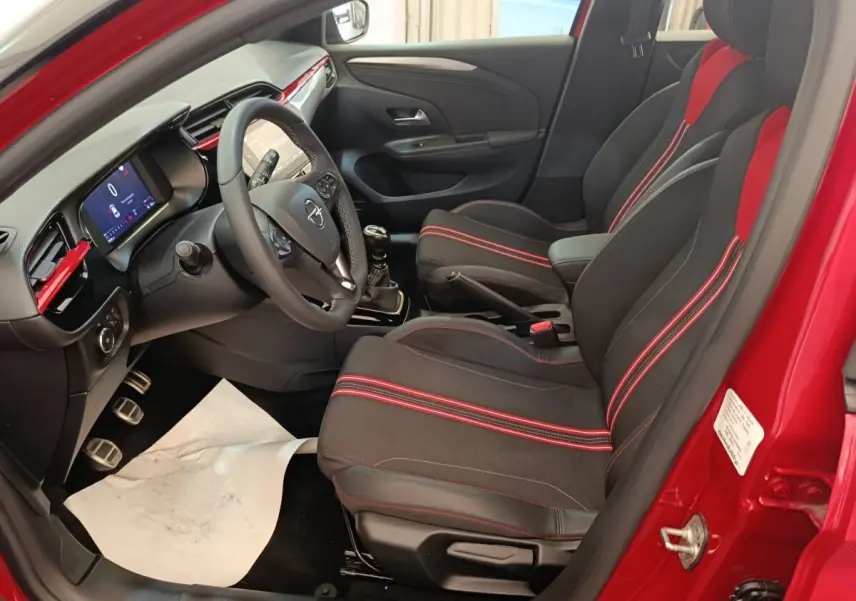 Intérieur de l’Opel Corsa rouge 2023, vue côté conducteur, sièges noirs avec surpiqûres rouges et tableau de bord digital.