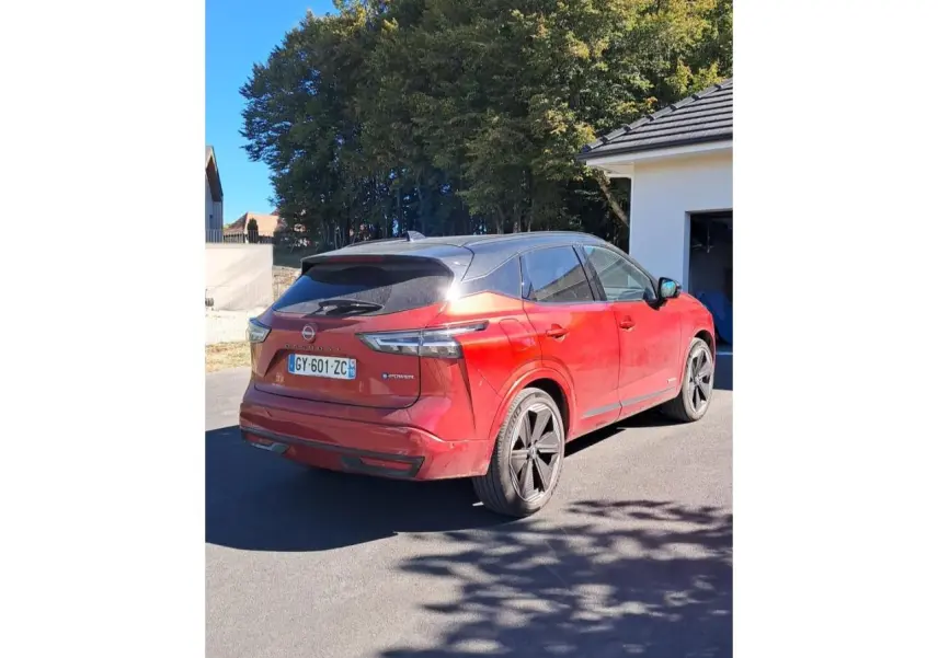 Vue 3/4 arrière droite d'un Nissan Qashqai 1.5 e-Power Tekna rouge foncé avec toit noir et jantes noires.