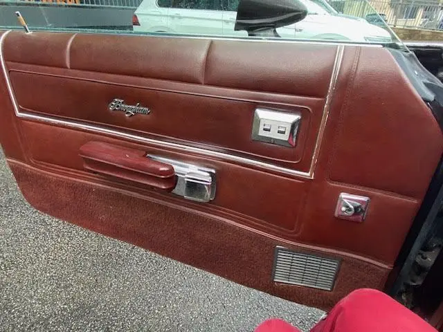 Gros plan sur la porte intérieure côté gauche en cuir bordeaux avec logo Ranchero et commandes électriques visibles.