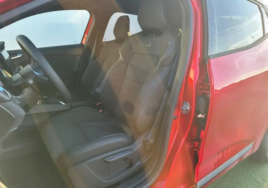 Vue intérieure côté conducteur d'une Renault Clio V rouge flamme avec sièges Esprit Alpine noirs brodés.