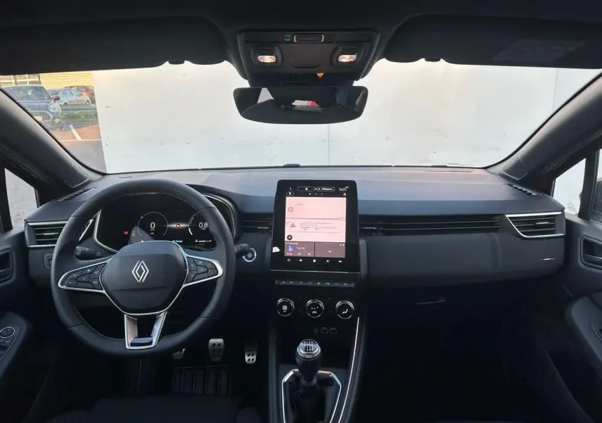 Vue intérieure avant de la Renault Clio V rouge flamme, volant multifonction, écran tactile vertical et levier de vitesse manuel.