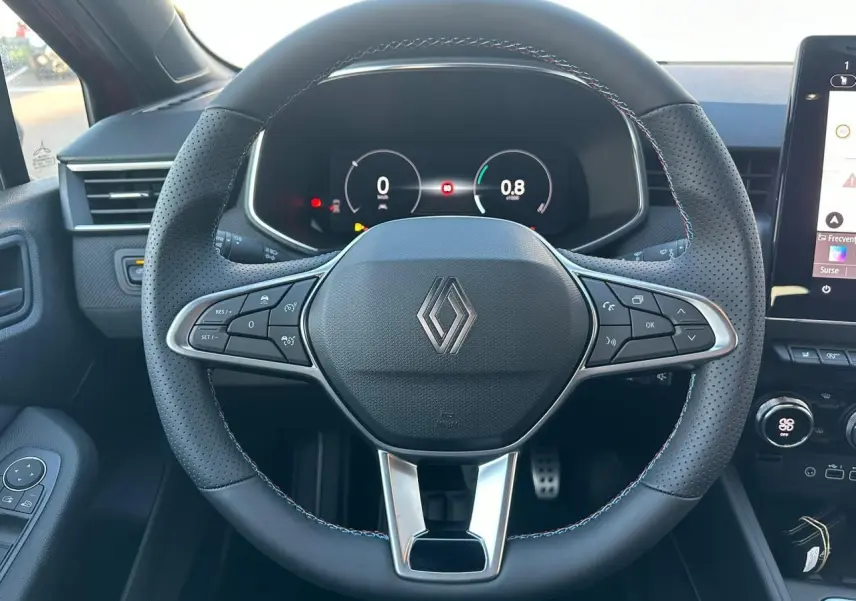 Volant multifonction noir avec surpiqûres tricolores et logo Renault, tableau de bord numérique d'une Renault Clio V rouge flamme métal.