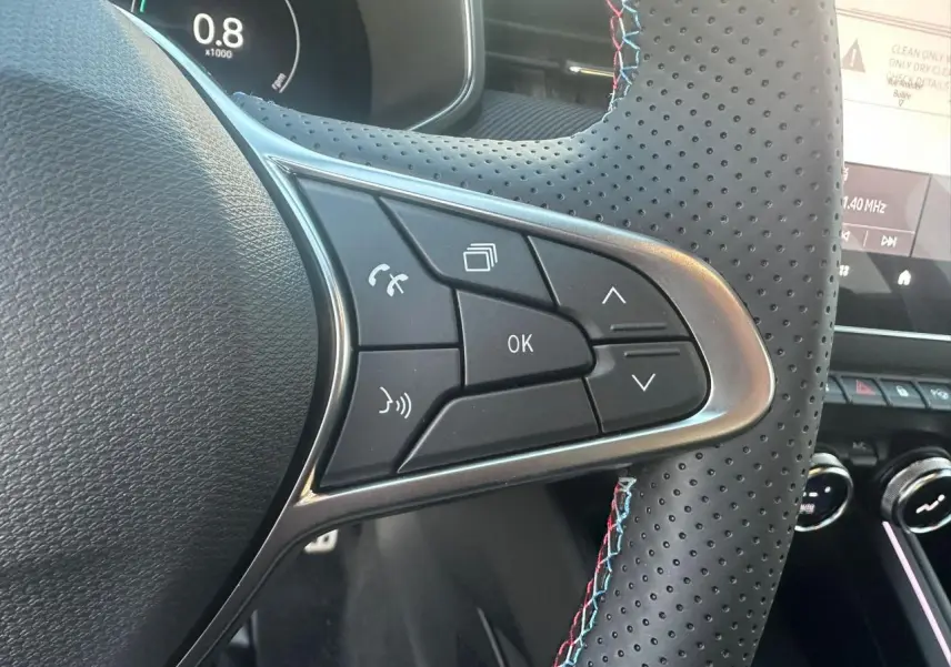 Gros plan sur les commandes du volant perforé avec surpiqûres tricolores de la Renault Clio V Esprit Alpine.
