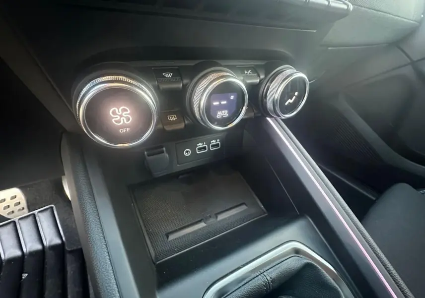 Gros plan sur la console centrale de la Renault Clio V rouge flamme, montrant les commandes de climatisation et ports USB.