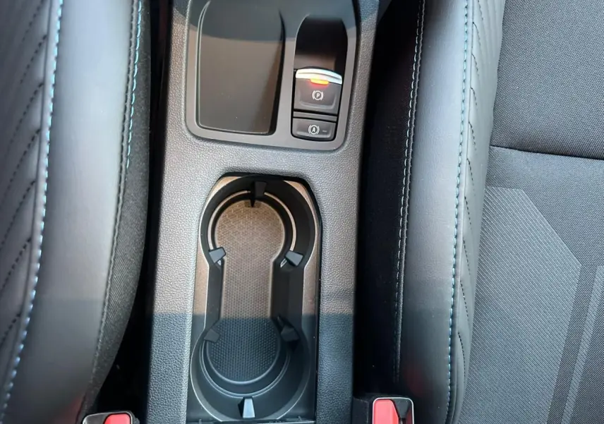 Gros plan sur la console centrale noire avec porte-gobelets et boutons de frein à main électrique dans une Renault Clio V rouge flamme.