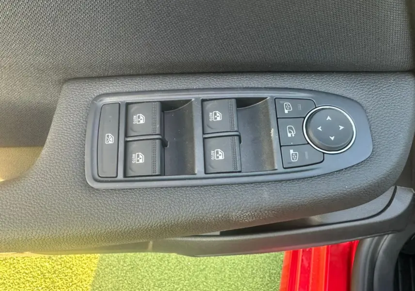 Commande des vitres électriques et réglage des rétroviseurs sur la porte côté gauche d'une Renault Clio rouge flamme.